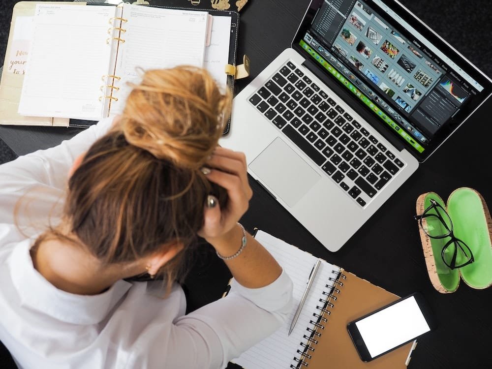 Woman holding her head looking overwhelmed at her computer, NLP coaching for ADHD